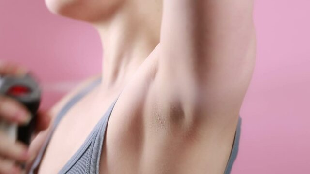 Hygiene and body care. A woman sprays deodorant to the armpit. Close-up of the armpit. Side view. Pink background. Protection against sweating