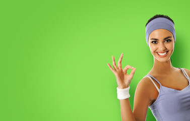 Young happy african american woman in sportswear showing okay hand sign gesture, isolated over green color background. Sporty model at studio shot. Health, beauty and fitness concept.