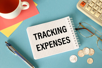 TRACKING EXPENSES is written on a notepad on an office desk