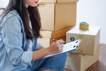 Asian woman checking and packing the carton box prepare to move to new house relocation shipping or...