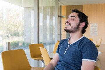 Happy young man breathing fresh air sitting in the lobby of an office building. Casual young man with a beard.