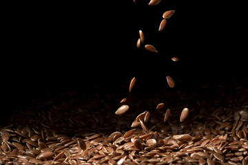 Close up of linseeds or flax seed on dark background with some falling spread in the right third of...