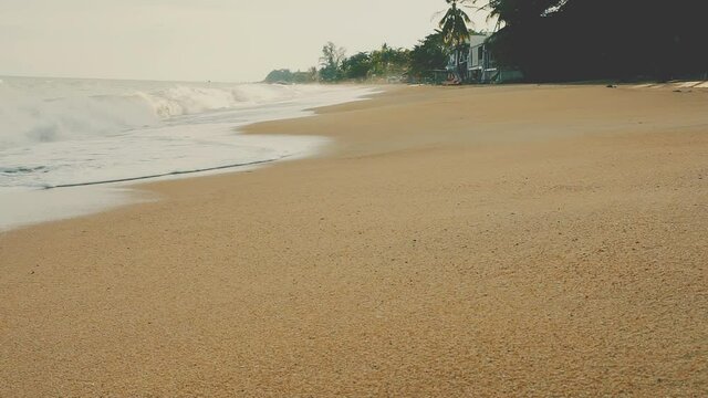 Coastline with surf and waves on a desert sandy tropical beach at sunset light