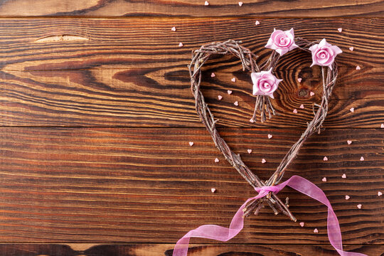Handmade branches heart with flowers and pink ribbon on wood background for loved one on Valentine day