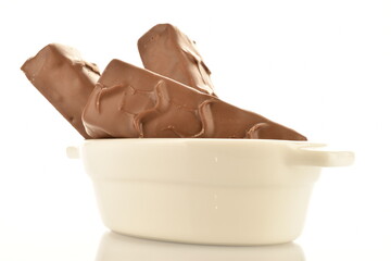 Several sweet chocolate bars in a ceramic white dish, close-up, isolated on white.
