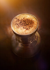 A cup of cappuccino coffee with milk, foam, and cinnamon on a blur wood background