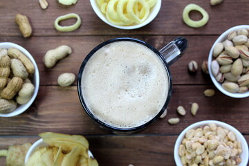 A mug of beer with foam is on the table next to snacks