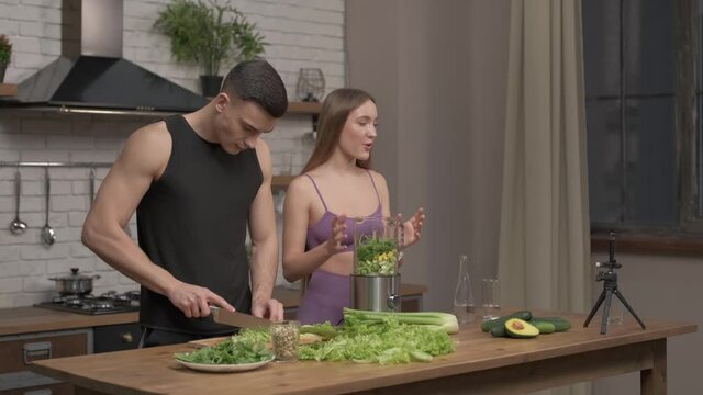 loving couple of athletes recording video food vlog about healthy cooking on phone camera in the kitchen at home. Vlogging, education and social media concept