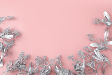 From above of silver flowers in shape of frame arranged on pink background in studio