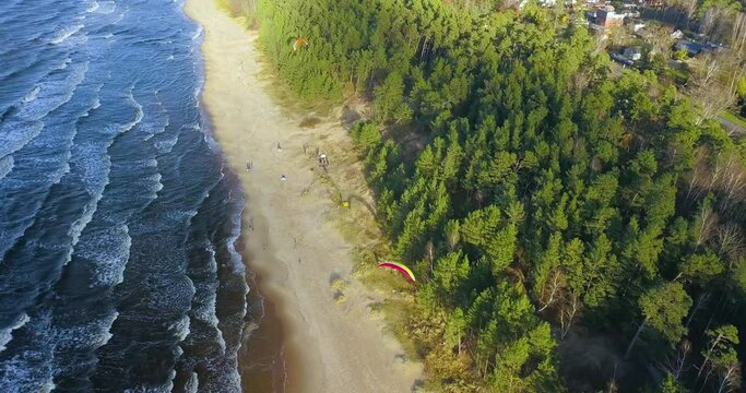 Aerial view of parasailers and tourists on beach with calm waves reaching the shore, sunny day. 4k.