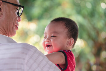 Portrait of grandfather and adorable expressions of Asian little baby  on nature background with copy space,Cute boy, 7 months old, crawling age, good smile and good mood. Healthy, big black eyes.