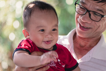 Portrait of adorable expressions of Asian little baby and grandfather on nature background with copy space,Cute boy, 7 months old, crawling age, good smile and good mood. Healthy, big black eyes.