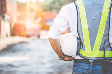 Back side view of Engineer wears reflection cloth and put walkie talkie in jeans packet and one arm hold white hardhat with left hand copy space. Concept Engineer work at construction site safety.