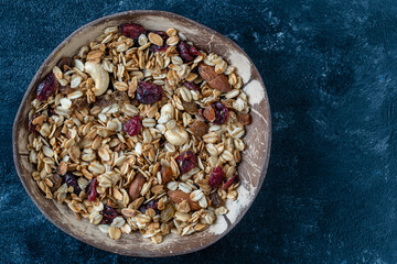 Obraz na płótnie Canvas Granola with oatmeal, dried fruit, honey, raisins, dry cranberry, almond and cashew nuts in a coconut bowl, close up, top view