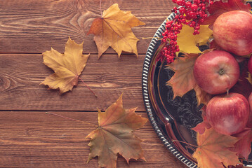 red apples,colorful autumn maple leaves on a metal tray on a wooden surface, top view
