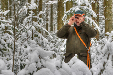 A hunter stands in the snowy forest and observes his hunting area through a small eyepiece.