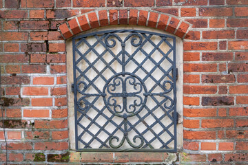 Forged lattice with pattern on closed window of an antique red brick rear. Architecture of medieval Europe
