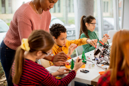 African American female science teacher with group of kids programming electric toys and robots at robotics classroom