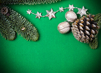 Christmas green background with fir branches, pine cone, stars and silver nuts.