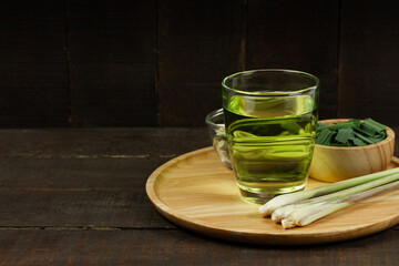 Lemon grass tea in glass and fresh lemon grass and green leaf in wooden bowl on wooden background. Healthy herbal drink concept dark tone.