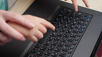 Top view of mother showing her child how to use computer keyoard. Boy with parent learnign and studying on laptop computer