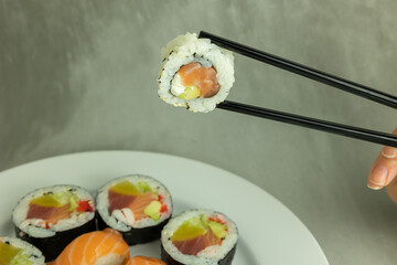 Hand holding sushi roll using chopsticks on gray background