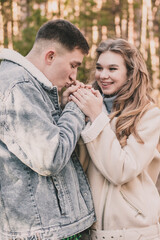 the guy holds the girl's hands and kisses them and the girl smiles while in the pine forest in winter