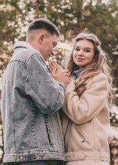 the guy holds the girl's hands and kisses them and the girl smiles while in the pine forest in winter