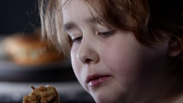 Baby girl at home eating fast food, breaded chicken drumstick. Close-up portrait of a little girl with plump cheeks eating food.