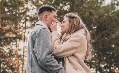 A girl holds a guy by the face with her hands and smiles at him while walking in a pine forest