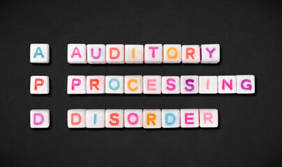 Auditory processing disorder and short form APD spelled out in colorful block letters on black...