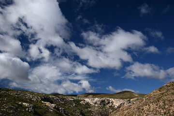Cielo con nubes. Cúmulos en cielo azul sobre monte desarbolado.