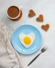 Heart shaped omelette on a light blue plate with coffee and bread