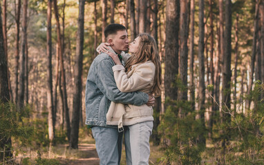 
the guy hugs the girl tightly and kisses her while in the pine forest