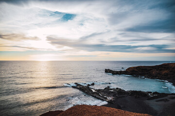 Coastline with dark rocks and calmed sea at sunset