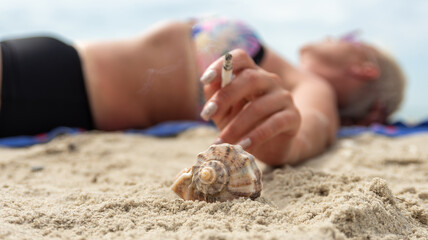 Smoking on the beach and shaking off cigarette ash into rapan