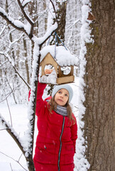 Girl hangs bird feeder on tree branch in winter snowy forest