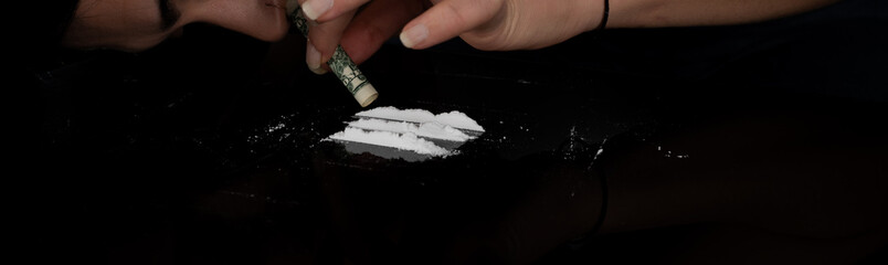 Drug addict woman snorting cocaine powder with rolled dollar banknote. Narcotics concept. Close-up...