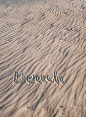 Naklejka na ściany i meble The word beach is written on the sand by hand. Beach season. Postcard. Shadows on the sand.