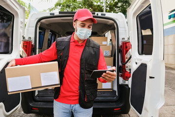 Delivery man with package and smartphone or digital scanner while wearing protective face mask at...