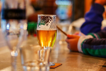 View of glass of bier with someone using the cellphone in the background
