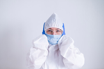 A woman in a protective suit and a medical mask covers her ears with her hands. I do not hear evil