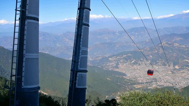 Red colored cable car moving up the hill near Chandragiri, Nepal with stunning panoramic view over Kathmandu valley and the snow-capped peaks of the Himalayas on sunny day.