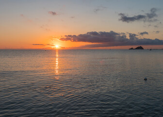 Sunrise with the red orange sun raising up from the sea with dark clouds at beach Spiaggia di Santa Maria Navarrese, Sardinia, Italy