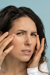 Close up of worried woman without makeup has signs of aging skin, checking crows feet troubled with...