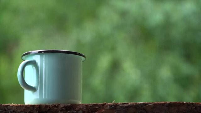 Closeup side view 4k video of light blue enamel metal mug isolated on green blurry natural bokeh background