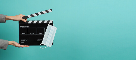 Hand hold black Clapper board or movie slate with face mask. it use in video production ,movies and cinema industry on blue and green or mint background.wear grey siut.