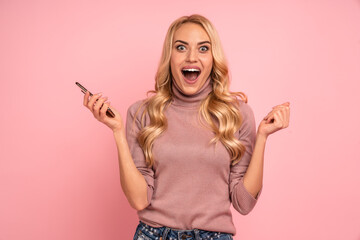 Portrait of a delighted young woman using mobile phone, isolated over pink background