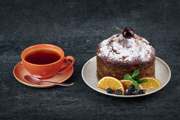 Fruity cake in plate with slices of dried orange and a cup of tea, closeup
