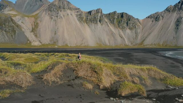 Epic drone view of the landscape in Stokksnes. Woman tourist walking on dunes in front of Vestrahorn mountain. Nature and ecology concept.